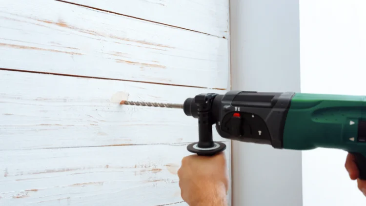 Using a hammer drill to drill a hole in a white wooden wall