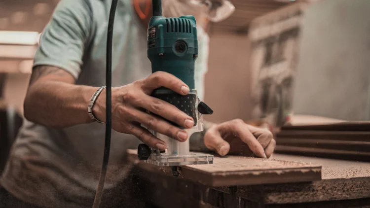 Worker using an electric woodworking tool on a wooden board.