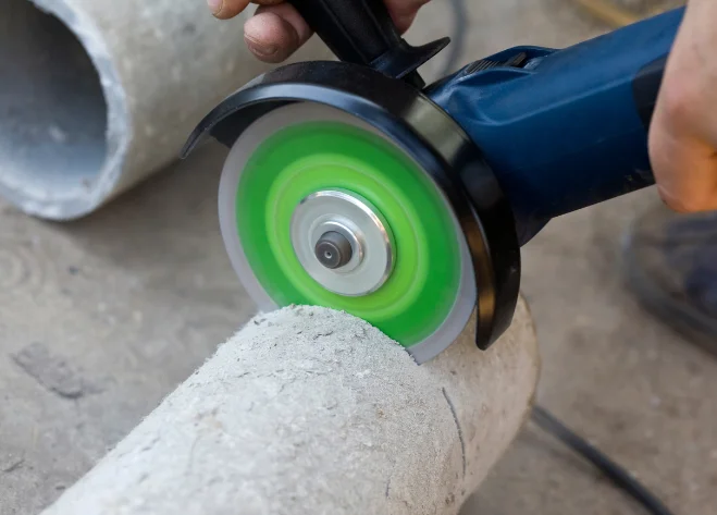 Using an angle grinder to cut a concrete pipe