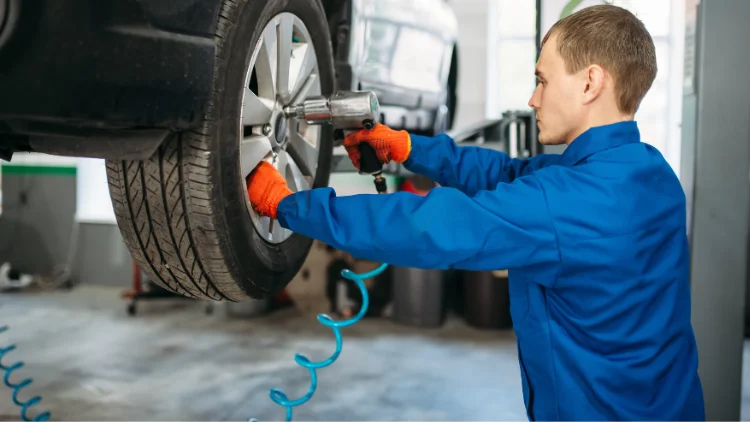 Mechanic using pneumatic impact wrench to remove wheel